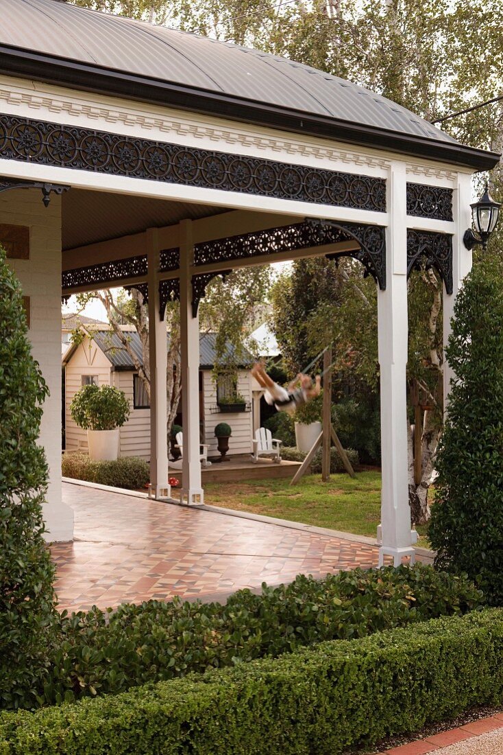 Porch with decorative frieze over veranda of Australian sandstone house built in 1890; play house and girl on swing in background