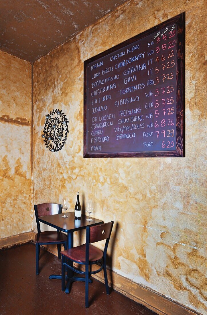 Weinbar mit Tisch, Stühlen und Schiefertafel mit Angeboten an der Wand