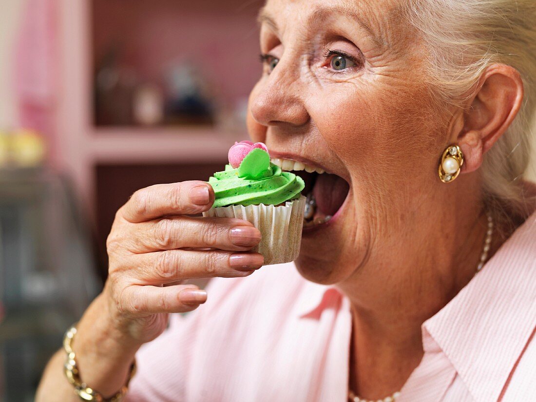 An old lady taking a big bite out of a cupcake