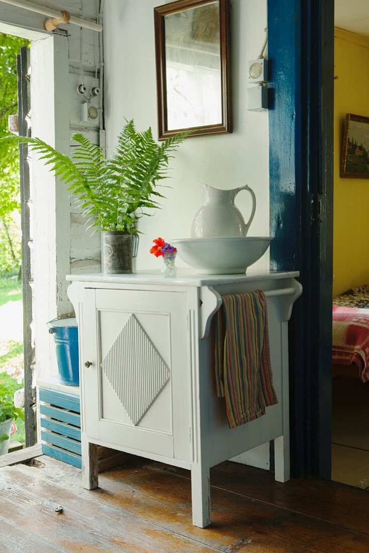 White wash basin and pitcher on half-height, white cabinet against wall between open exterior door and interior door