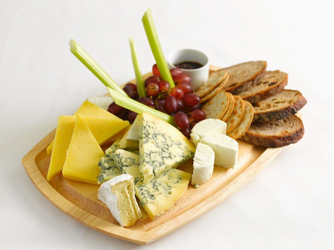 A cheese platter with bread, grapes and celery