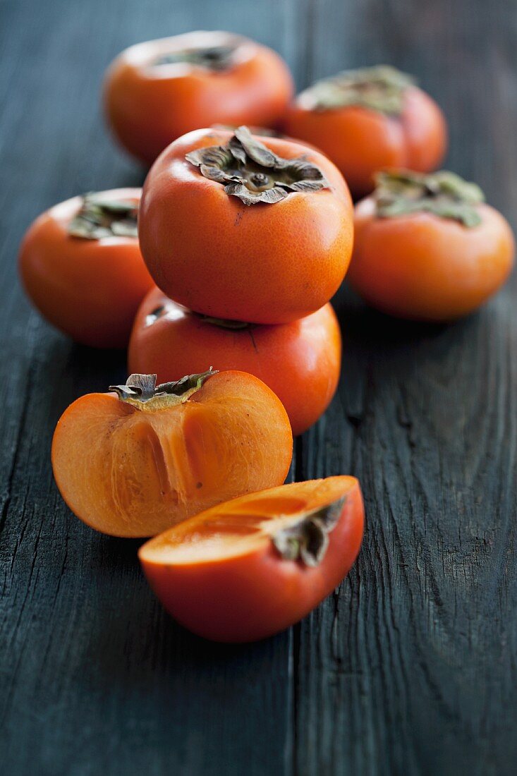 Fresh persimmons, whole and halved, on a wooden surface