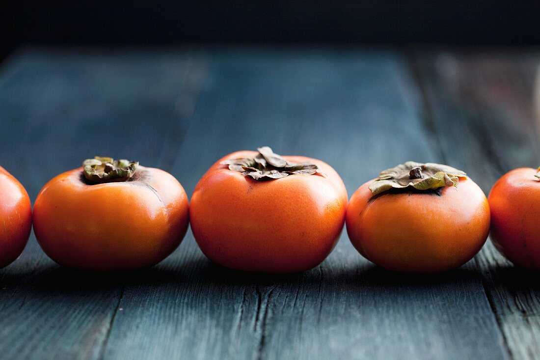 A row of persimmons on a wooden surface