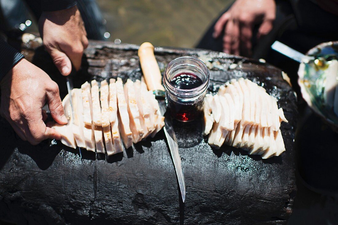 Two men preparing fresh fish on a tree trunk