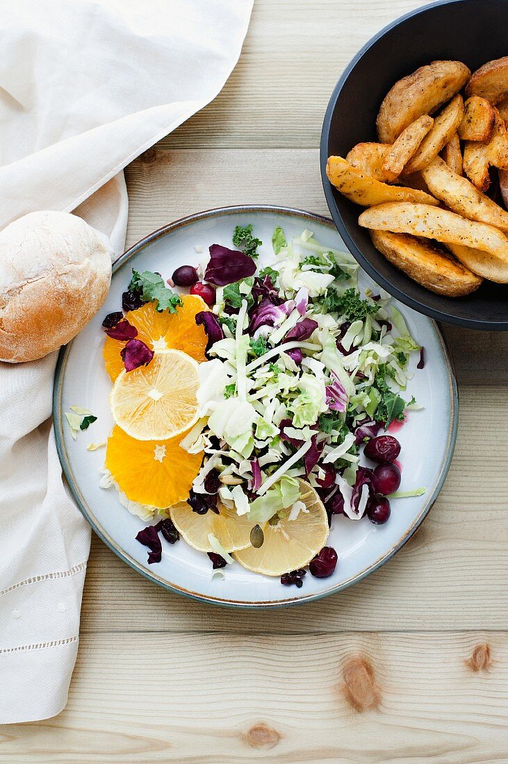 A mixed leaf salad with citrus fruits, cranberries and a side of chips