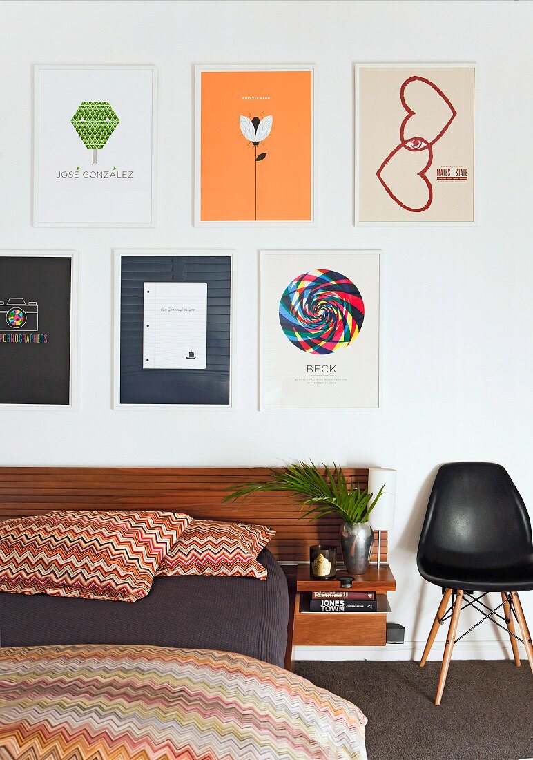 Modern bed with Missoni bed linen and classic shell chair against wall below framed pictures