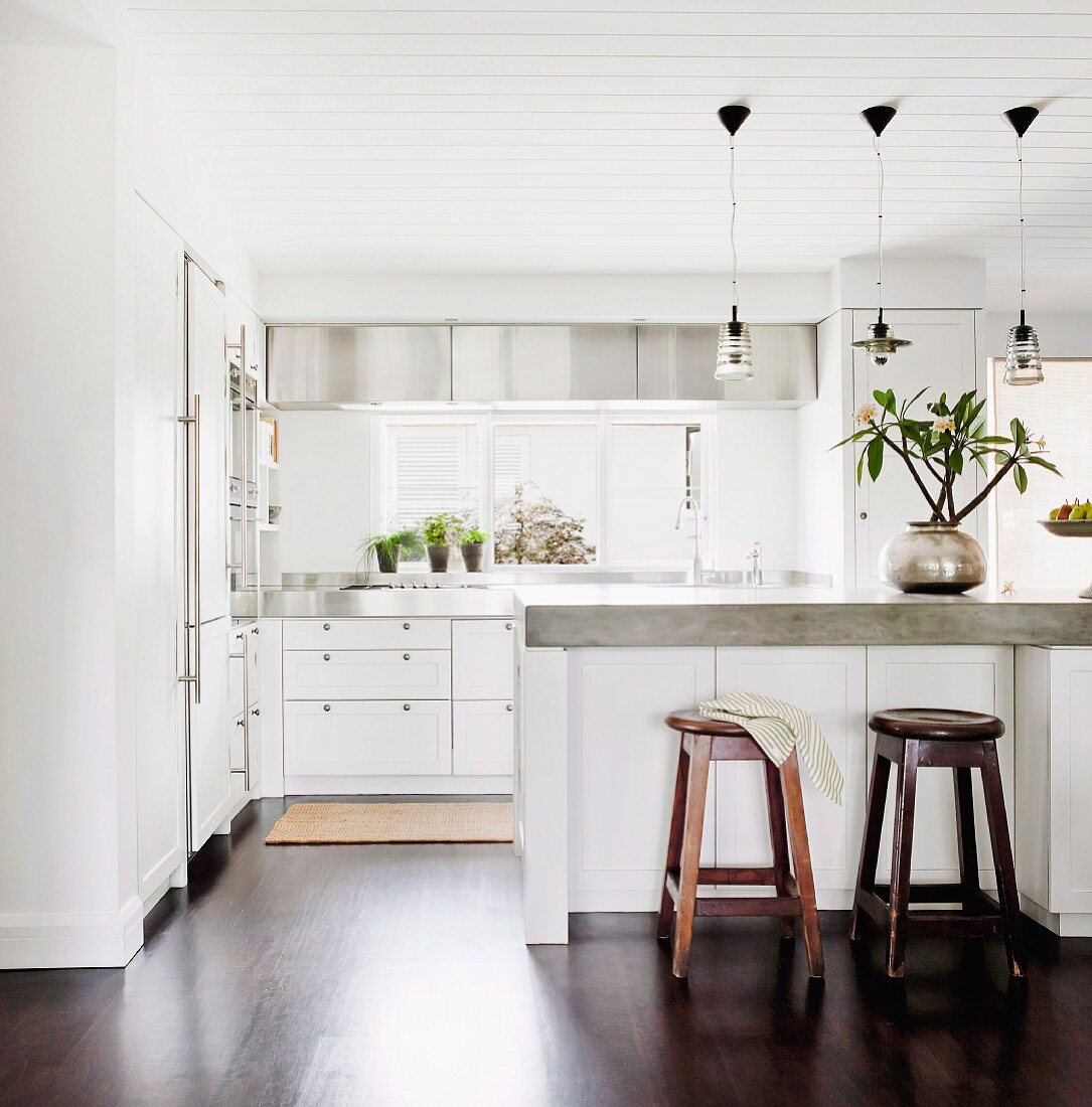 Wooden barstools at counter with concrete worksurface below simple pendant lamps in open-plan kitchen