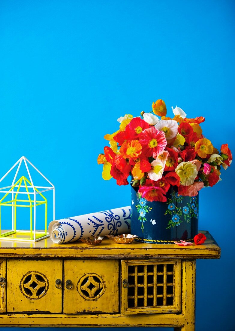 Colourful bouquet and roll of wallpaper on vintage cabinet against blue wall