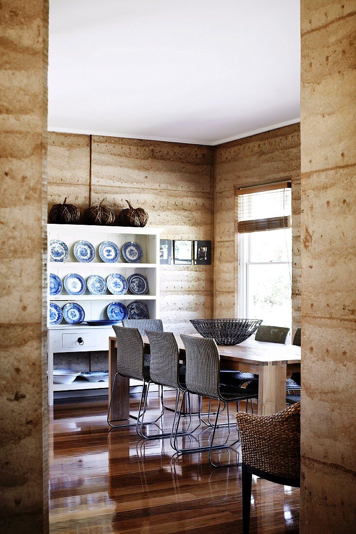 Collection of blue and white plates on shelving in dining room with unrendered, clay walls constructed using modern technique