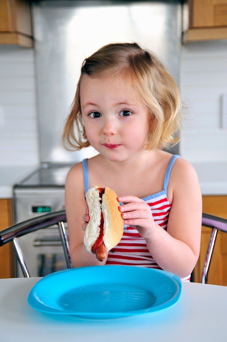 A little girl eating a hot dog