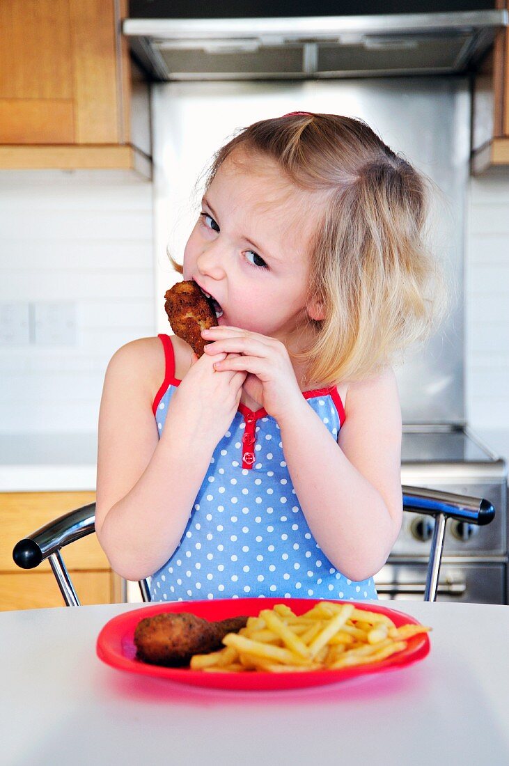 A little girl eating a chicken leg with chips