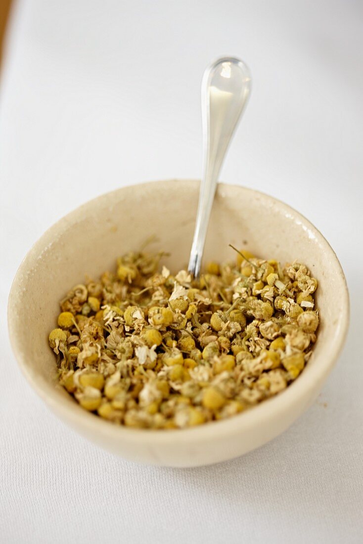 Dried camomile flowers in a bowl with a spoon