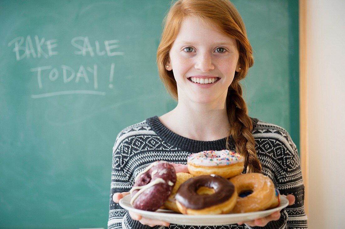 A girl holding a plate of doughnuts