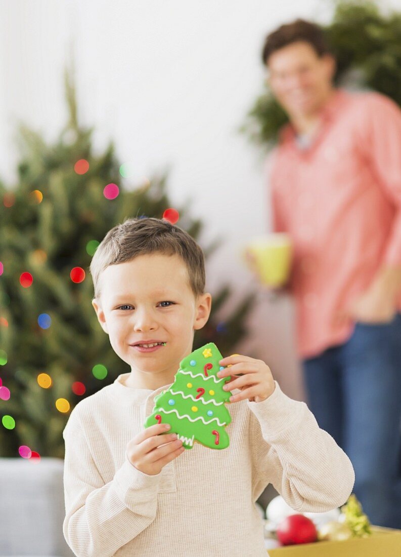 A boy holding a Christmas tree-shaped biscuit