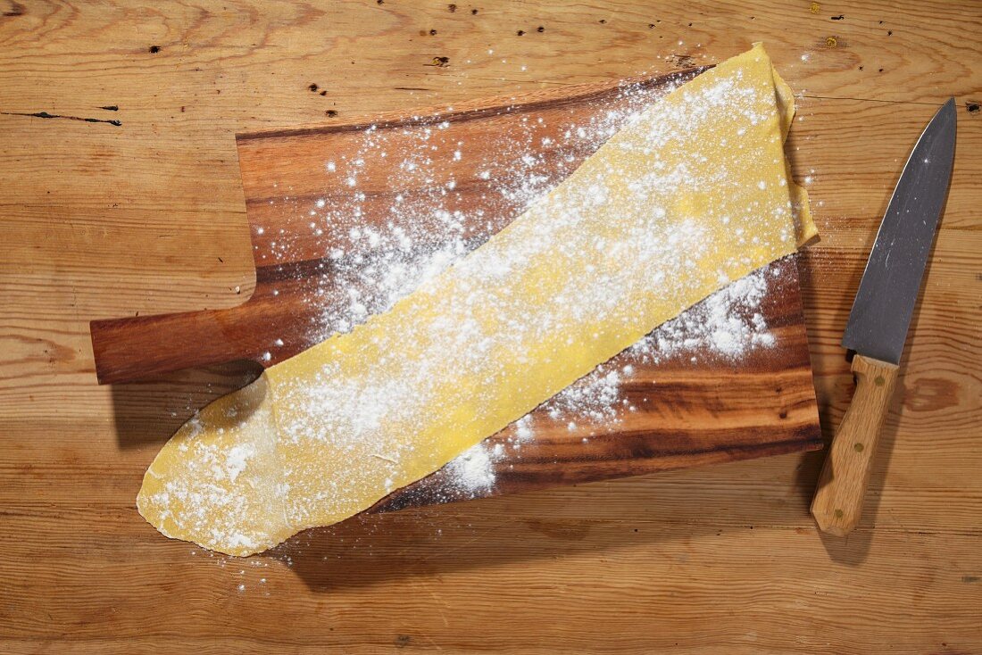 Rolled out pasta dough dusted with flour on a chopping board