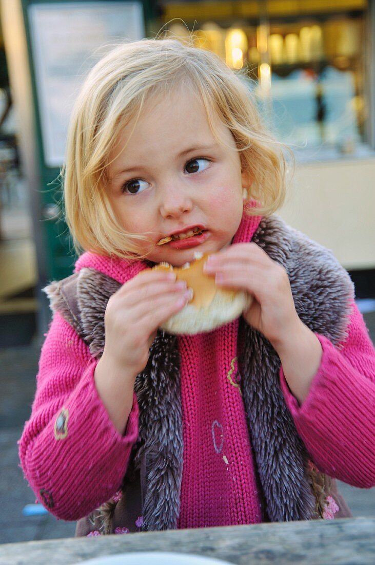 A little girl eating a bread roll at a market
