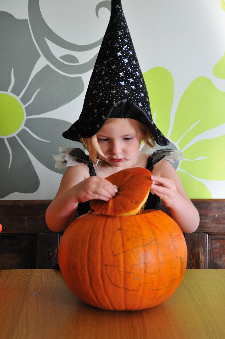 A little girl in a Halloween costume with a pumpkin