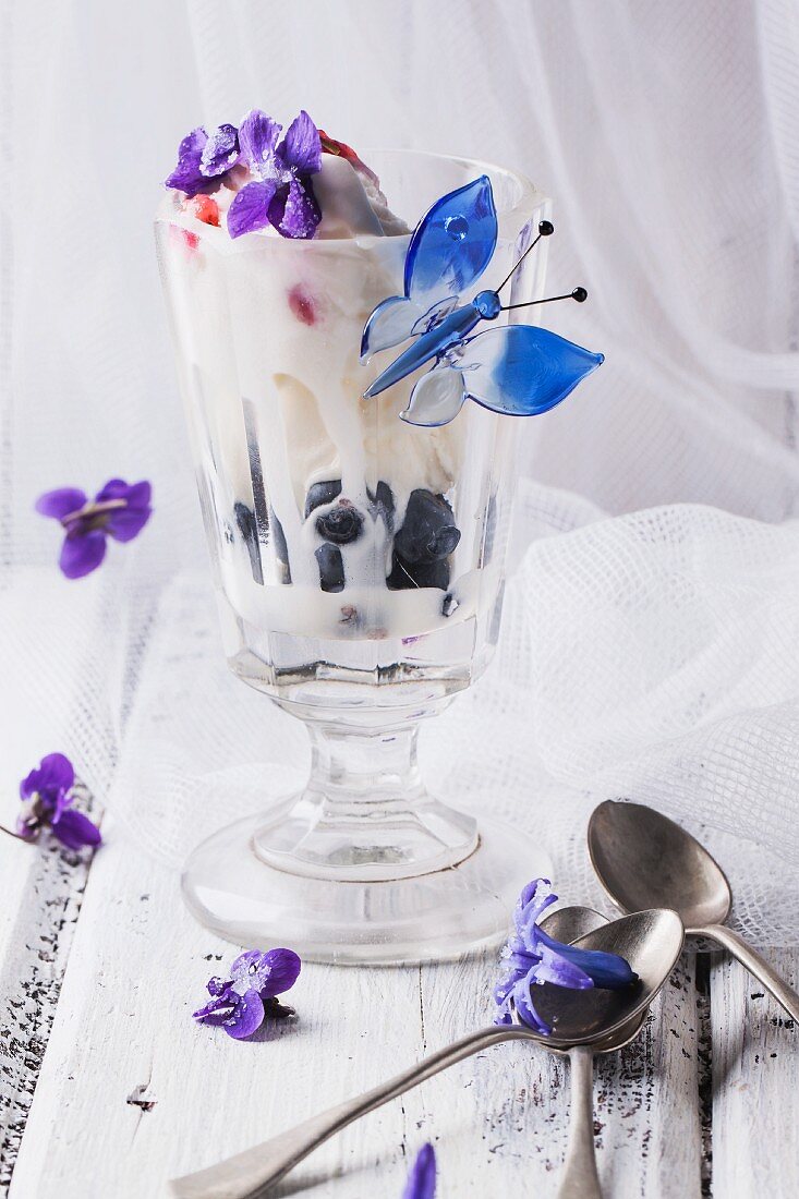 Eisbecher mit Vanilleeis, Fruchtgelee und Heidelbeeren, Deko gezuckerte Veilchenblüten