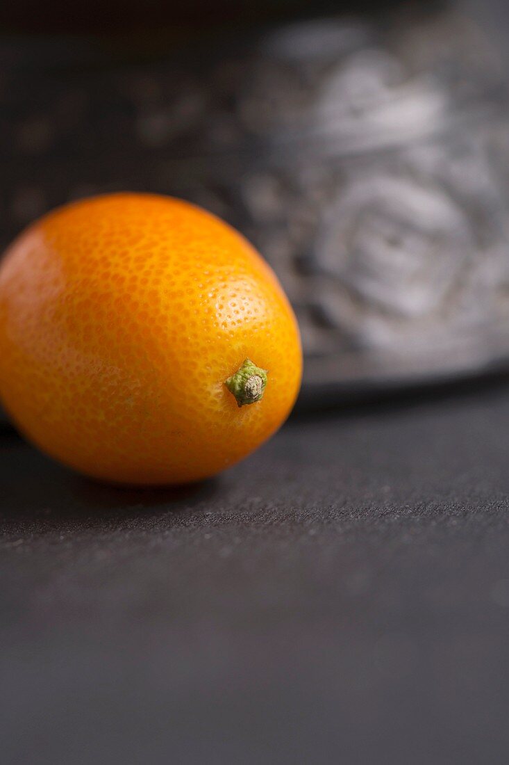 A single kumquat with a terracotta container in the background