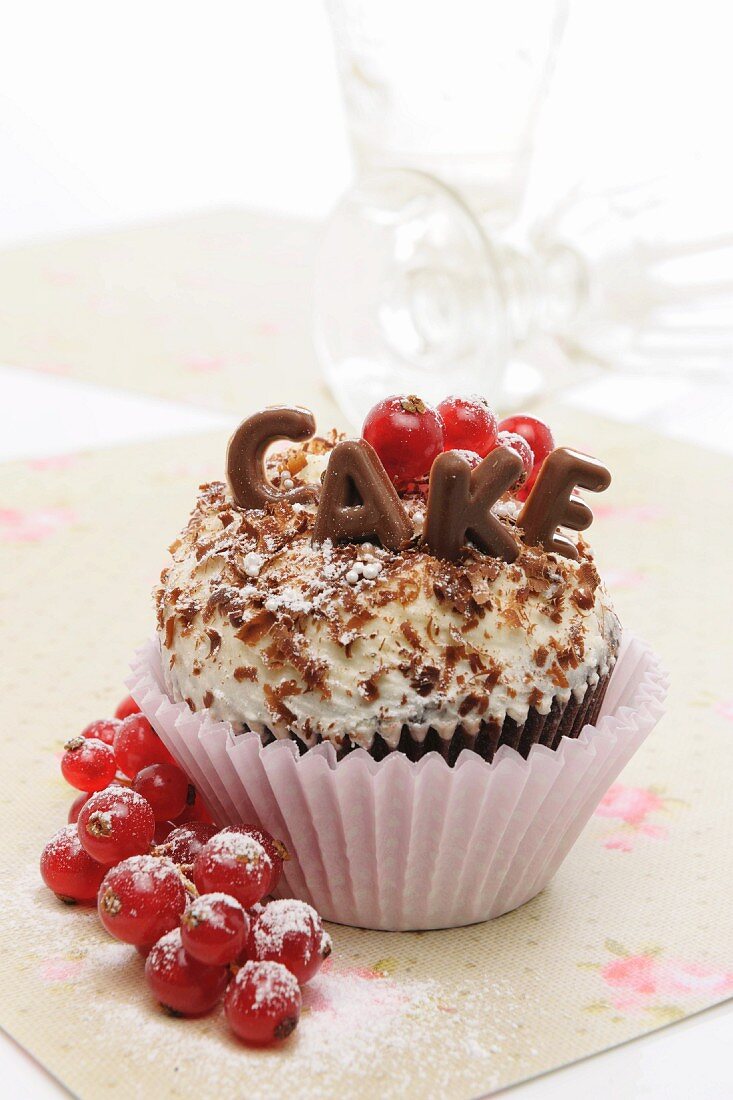 A cupcake decorated with chocolate letters and redcurrants