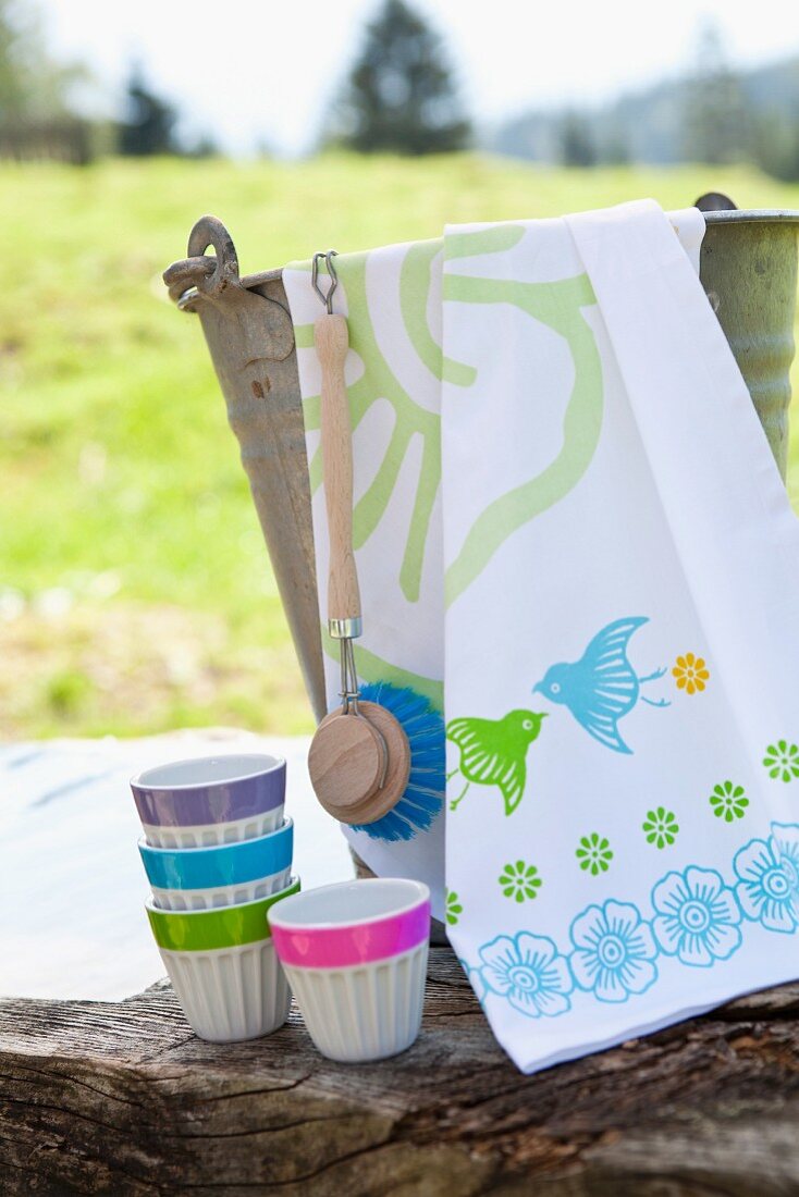 White pudding cups with edges in various neon colours and tea towel on zinc bucket arranged on weathered wooden block