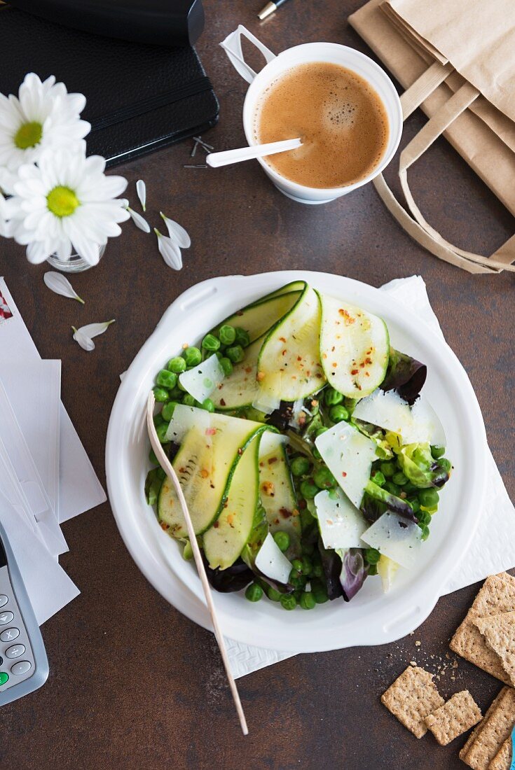 Pea and courgette salad with Parmesan, crisp bread and a cup of coffee in an office