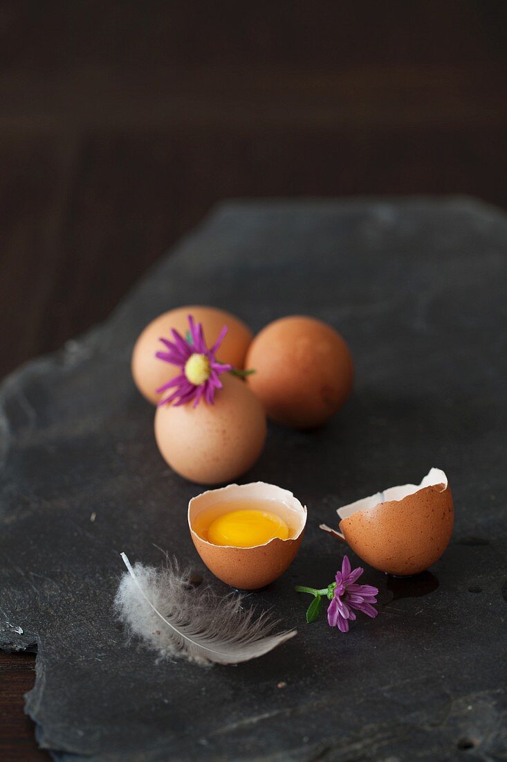Eggs, whole and cracked, with a feather and a flower on a black stone