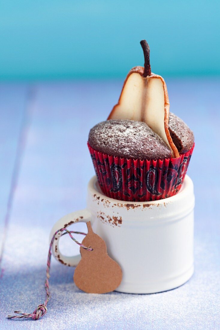A chocolate muffin decorated with a pear and icing sugar