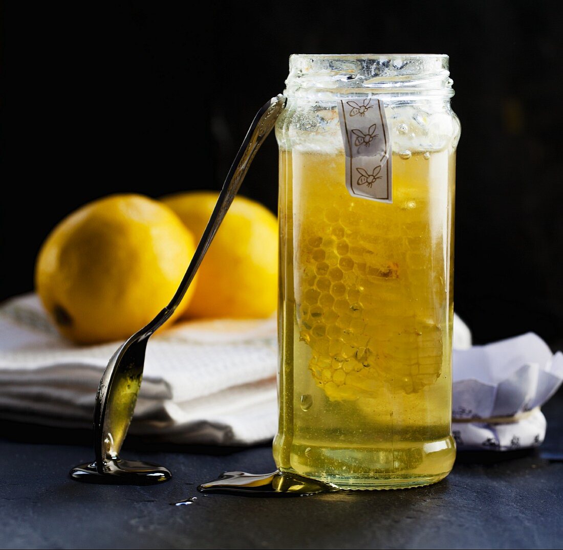 Honig mit Honigwabe im Glas vor Zitronen