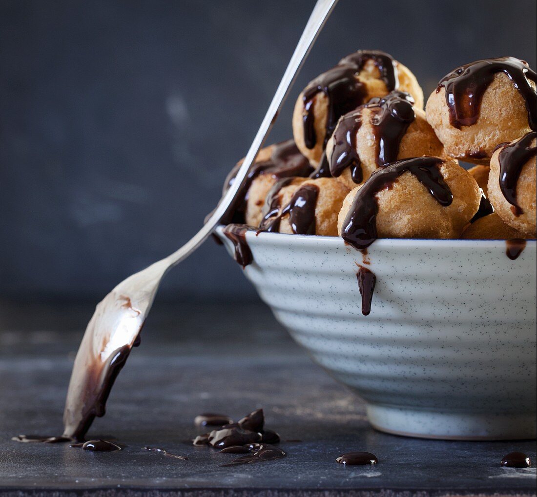 Profiteroles mit Schokoladensauce in Schale mit Löffel