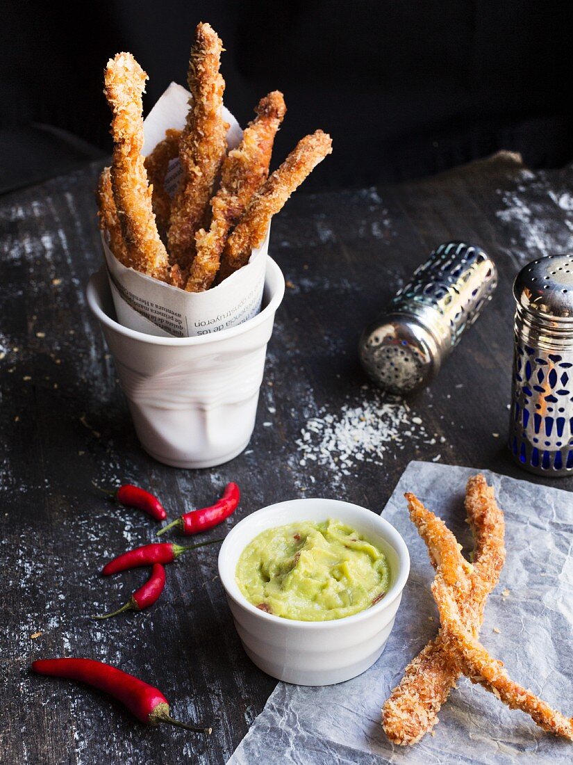 Baked chicken sticks in a cup with guacamole on a black wooden table