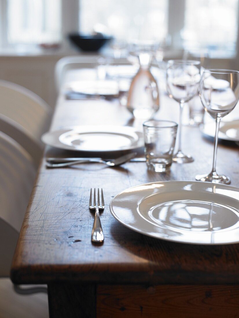 Wooden table set with white plates and glasses (detail)