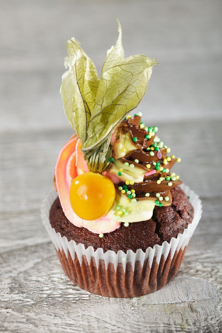 A chocolate cupcake with buttercream, sugar sprinkels and a physalis