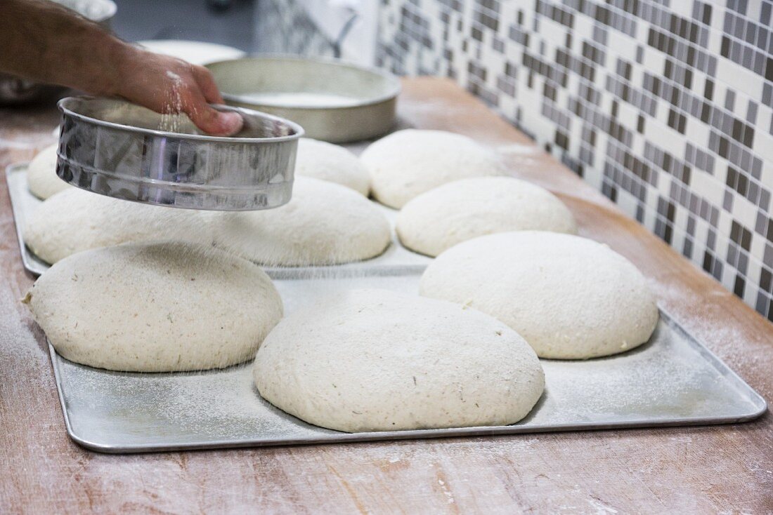 Hands sprinkling flour on loaves of unbaked bread