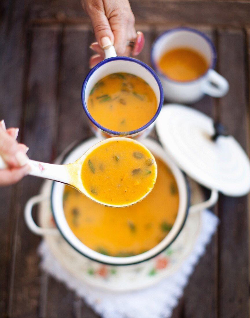 Süßkartoffelsuppe mit Ingwer wird in Emaillebecher geschöpft