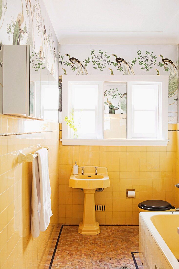 Vintage-Bad mit Standwaschbecken vor gelben Wandfliesen, darüber Schablonenmalerei mit Vogelmotiv