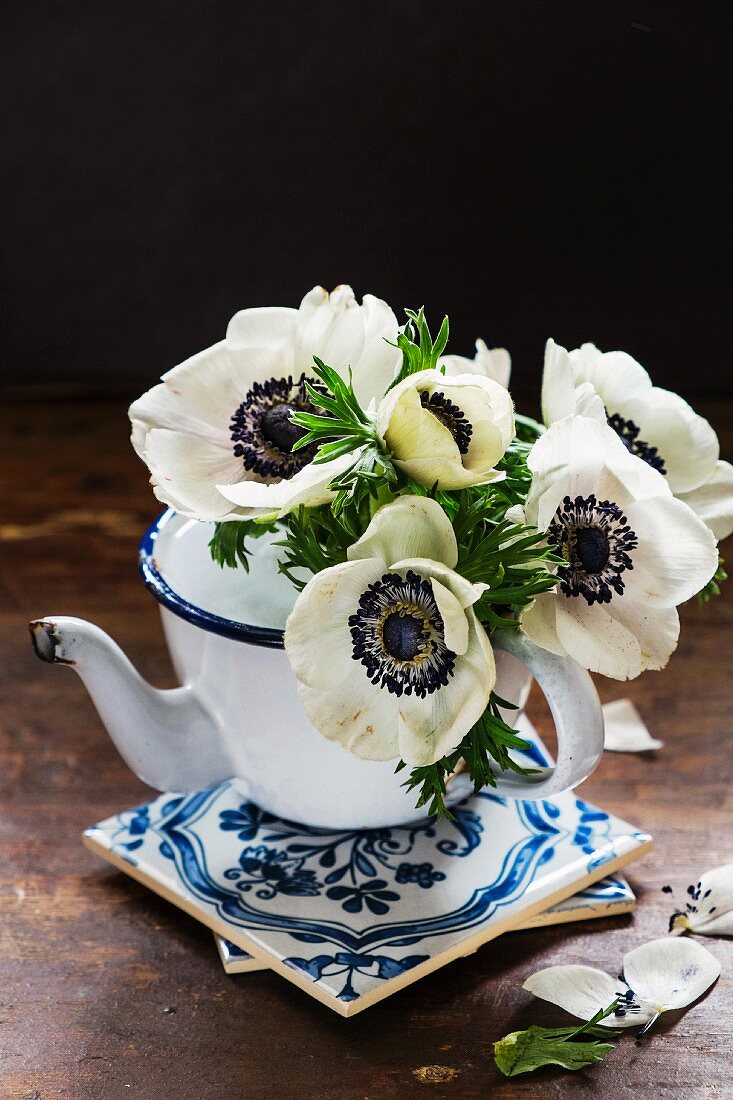 White anemones in an old-fashioned metal jug on a stack of tiles