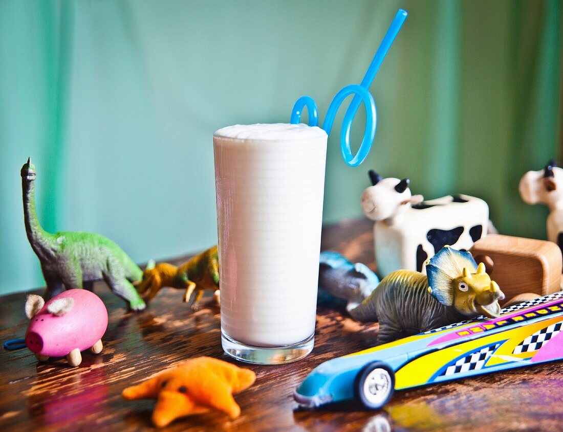 A vanilla milkshake on a wooden table surrounded by toys