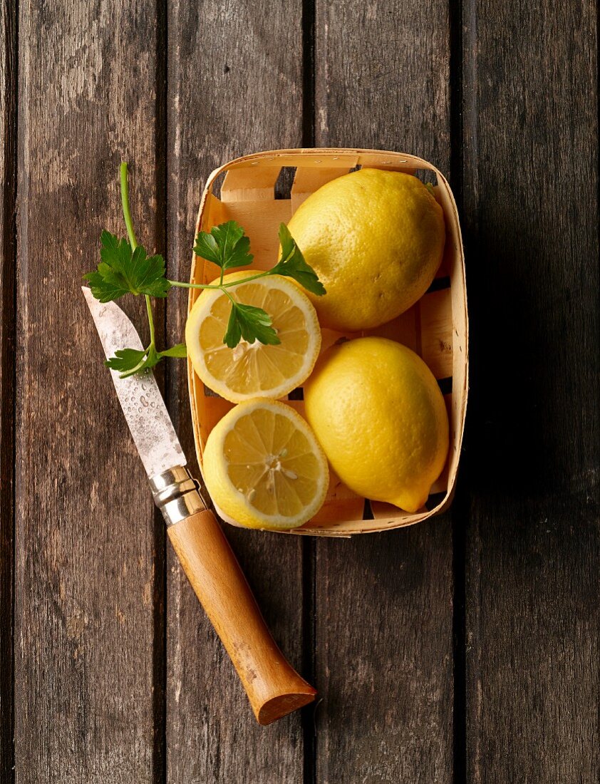Zitronen und Petersilie im Spankorb auf Holzuntergrund