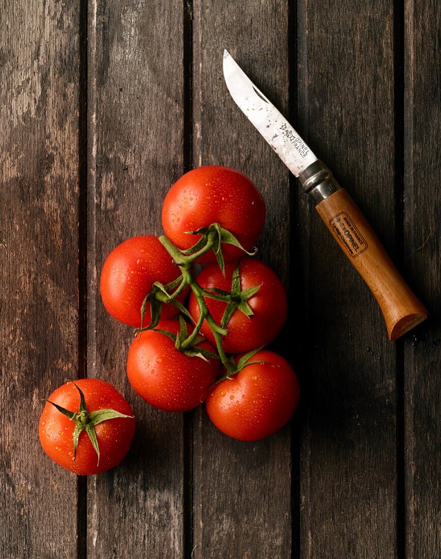 Vine tomatoes and a knife on a wooden surface