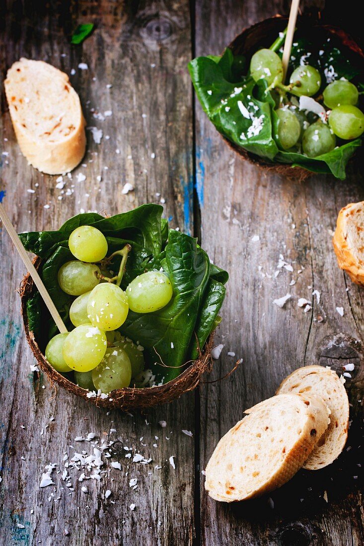 Grape and spinach salad served in a coconut shell on a wooden surface