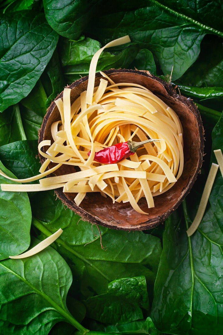 Tagliatelle and a chilli pepper in a coconut shell on a bed of spinach leaves