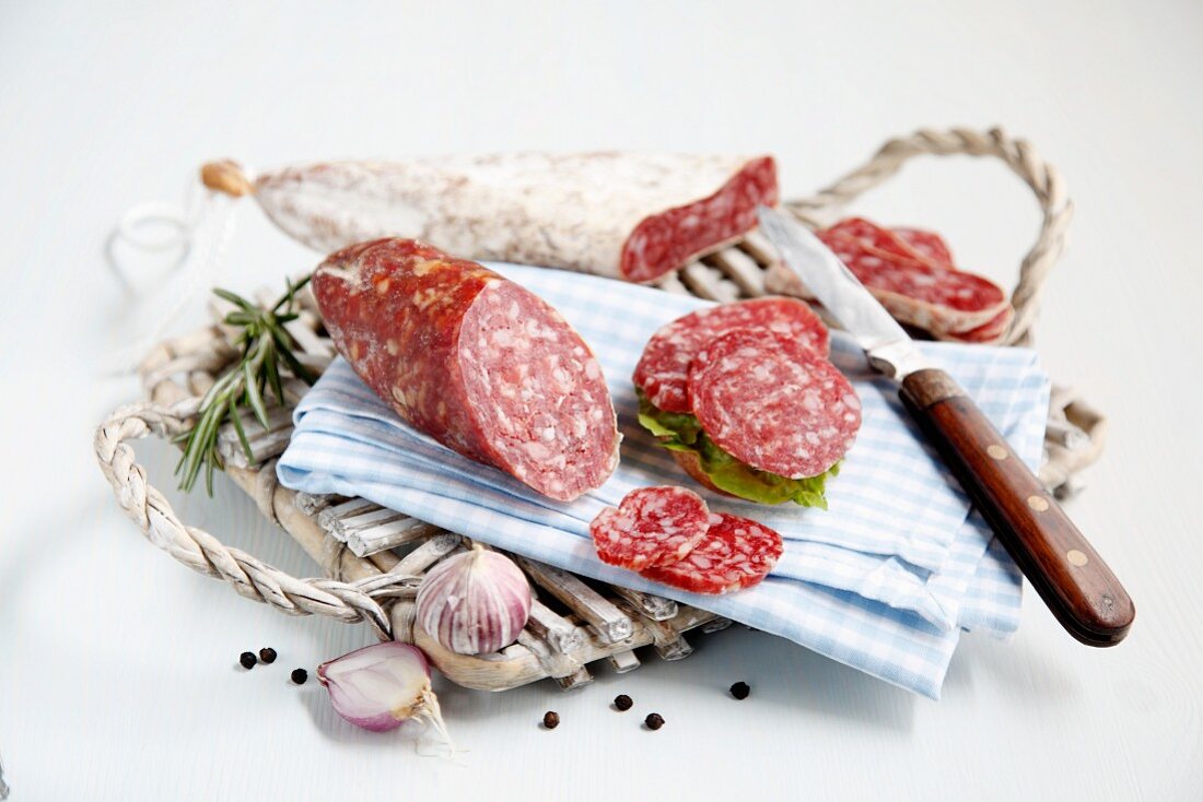 Salami on a board with a blue and white checked napkin, a knife and onions