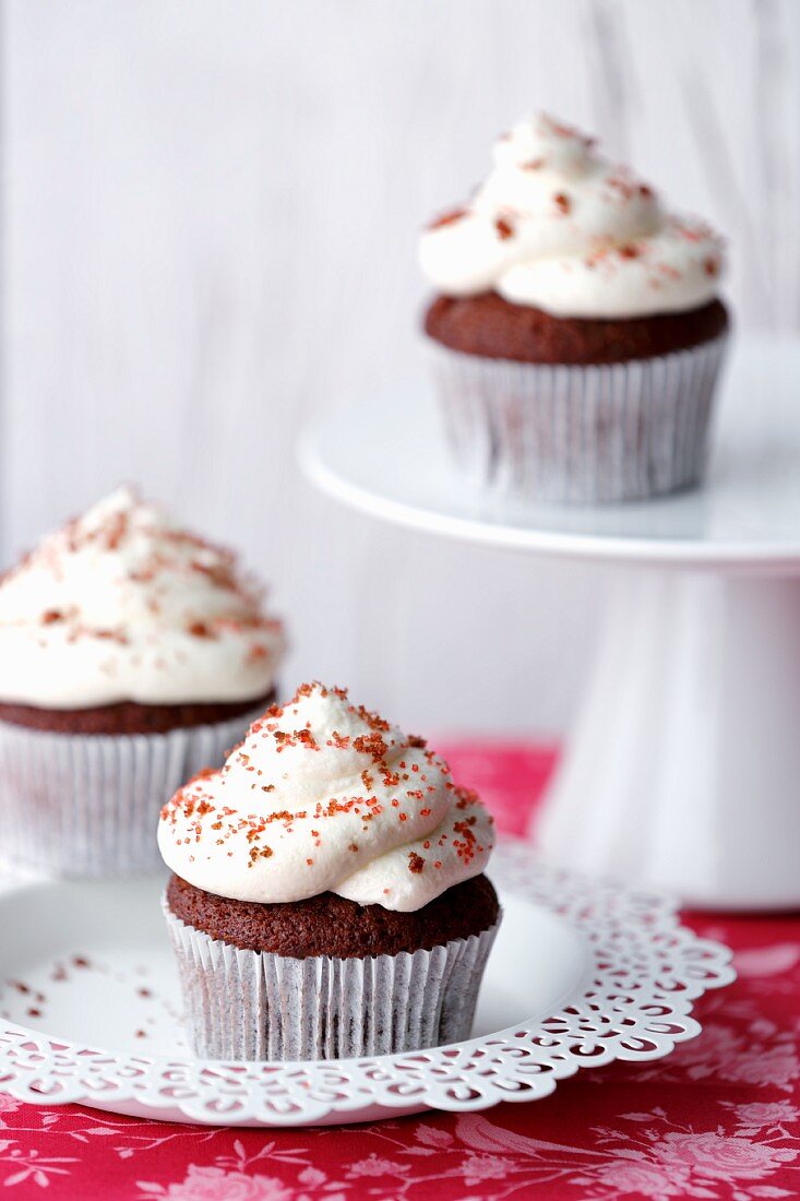 Three Red Velvet cupcakes on a plate and on a cake stand