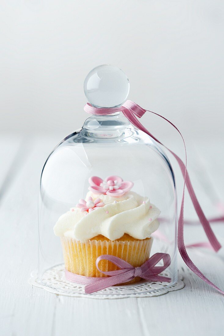 A cupcake decorated with pink sugar flowers under a glass cloche