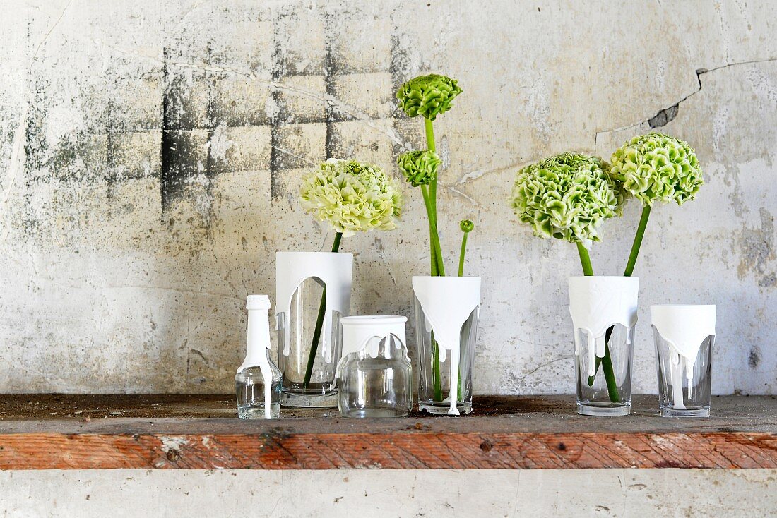 Craft idea - glass vessels dipped in white paint holding flowers on surface against weathered stone wall