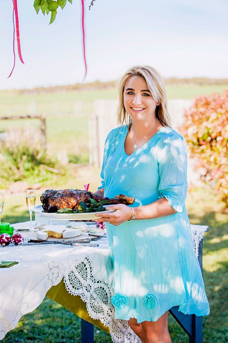 Woman serving braised leg of lamb at table in garden