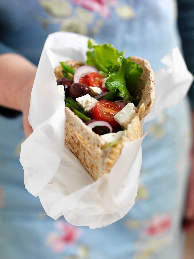A woman holding a pita bread filled with Greek salad
