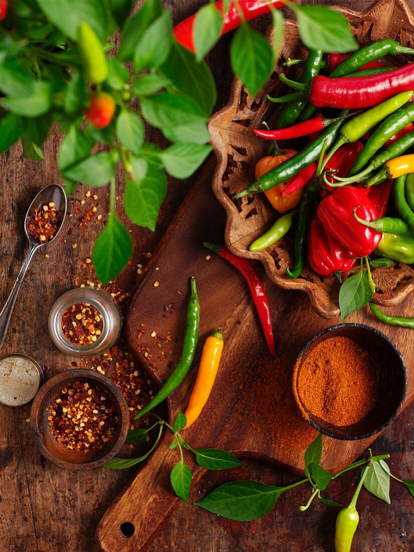 Various chilli peppers, chilli flakes and powder on a wooden board