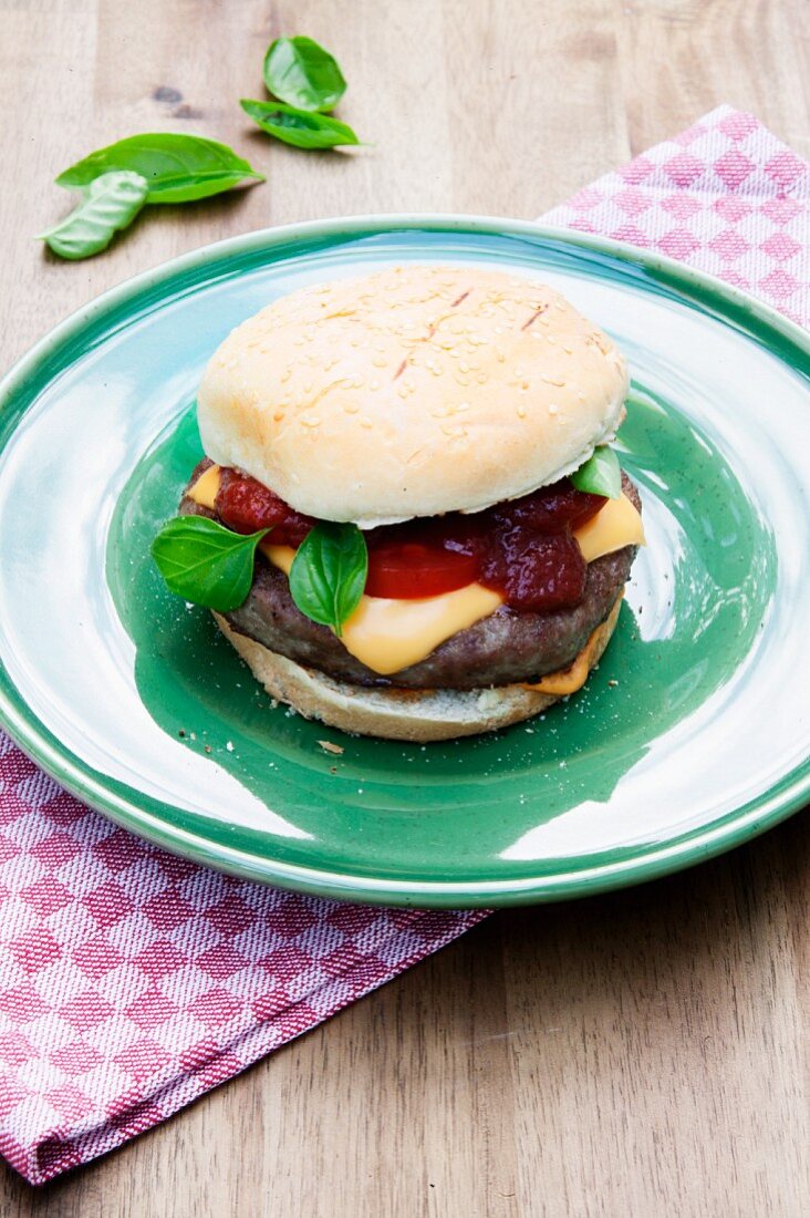 Gegrillter Cheeseburger mit Tomate und Basilikum auf grünem Teller